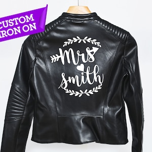 Könnte beinhalten: Schwarze Lederjacke mit einem weißen Bügelbild, auf dem "Mrs. Smith" mit einem Pfeil und einem Herzen steht.