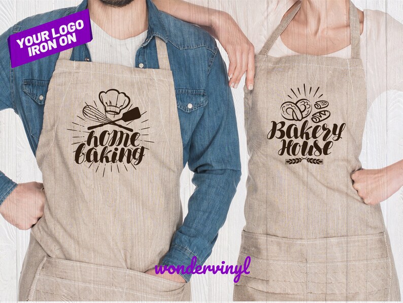 K&ouml;nnte beinhalten: Zwei braune Leinensch&uuml;rzen mit B&uuml;gelmotiven. Eine Sch&uuml;rze zeigt einen Kochhut, einen Schneebesen und einen Spatel mit dem Text "home baking". Die andere Sch&uuml;rze zeigt ein Design mit Br&ouml;tchen mit dem Text "Bakery House".