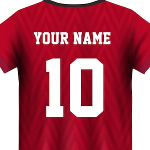 Può includere: Maglia da calcio rossa con un motivo a chevron bianco. Sul retro della maglia è presente il testo "YOUR NAME" e il numero "10" in bianco.