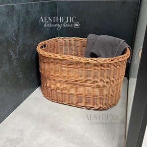 May include: A brown wicker basket with a gray towel inside. The basket is sitting on a gray tiled floor in a bathroom.