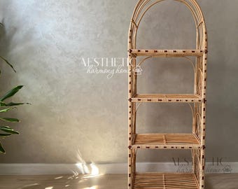 May include: A natural woven rattan shelf unit with four shelves. The shelf has a rounded arch top and is made of light brown rattan with dark brown accents.