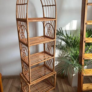 May include: A tall, arched, natural woven rattan shelf unit with four shelves. The shelf unit is made of light brown rattan and has a natural finish.