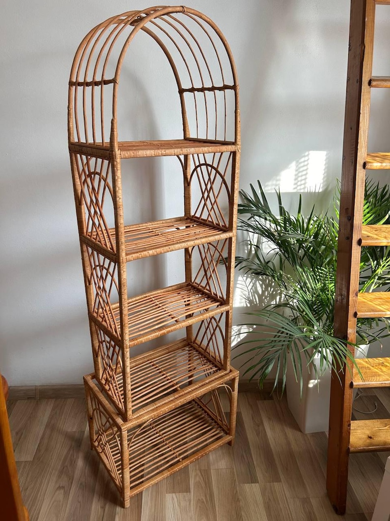 May include: A tall, arched, natural woven rattan shelf unit with four shelves. The shelf unit is made of light brown rattan and has a natural finish.