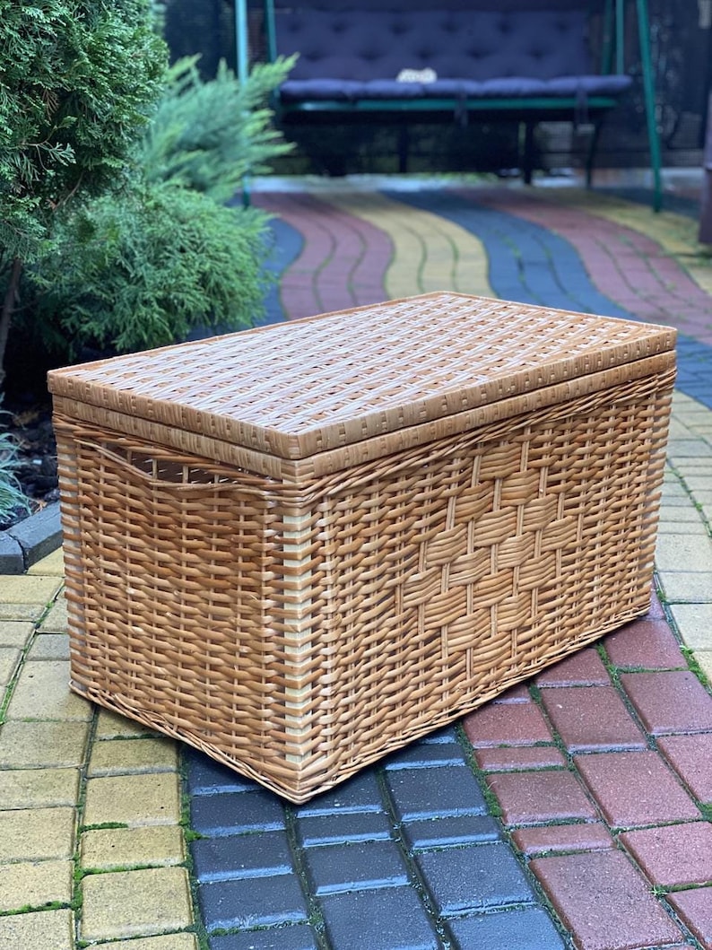 May include: A large, rectangular wicker storage basket with a lid. The basket is made of natural woven wicker and has a light brown color.