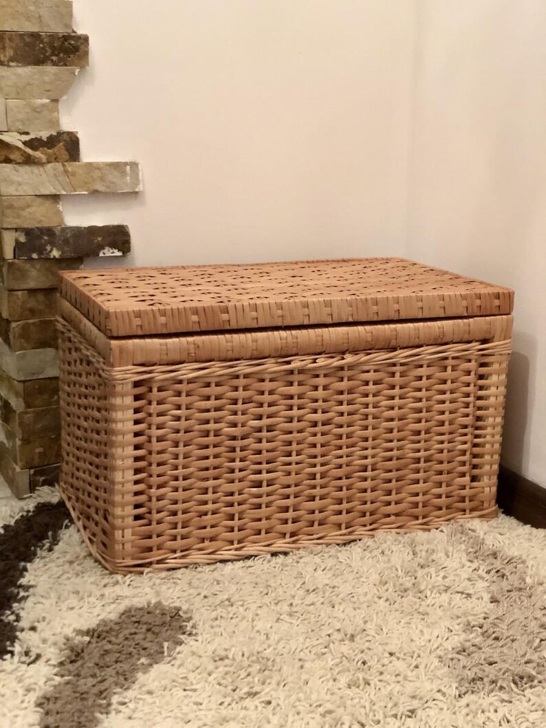 Puede incluir: Una cesta de almacenamiento de mimbre tejido con tapa. La cesta es de color marr&oacute;n claro y tiene una forma rectangular.