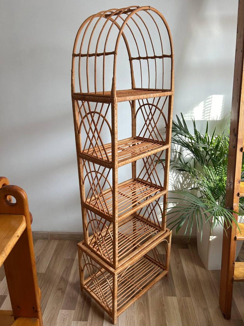 May include: A tall, arched, woven wicker shelf unit with four shelves. The shelf unit is made of natural brown wicker and has a rustic, bohemian style.