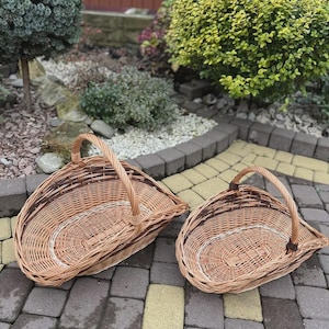 May include: Two woven wicker baskets with a natural light brown finish and a single arched handle. The baskets feature a distinctive asymmetrical, sloped shape with a flat base and a curved rim, showcasing a detailed interlaced willow pattern.