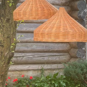 Pu&ograve; includere: Due luci a sospensione in vimini intrecciato appese a un soffitto in legno. Le luci sono di colore arancio chiaro e hanno una forma arrotondata a cupola.