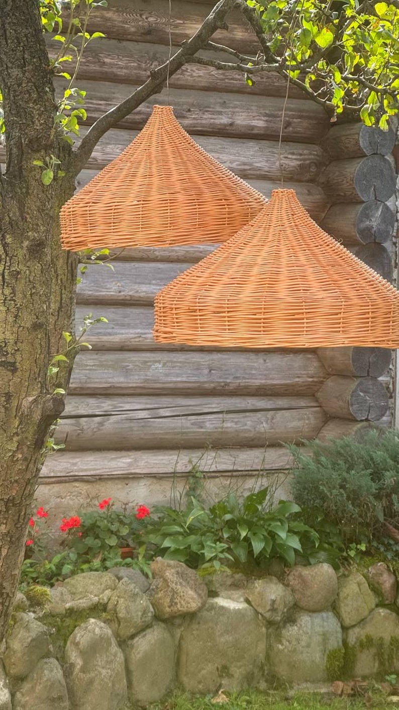 Pu&ograve; includere: Due luci a sospensione in vimini intrecciato appese a un soffitto in legno. Le luci sono di colore arancio chiaro e hanno una forma arrotondata a cupola.