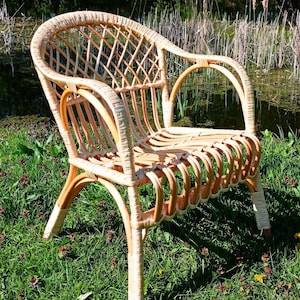 May include: A wicker chair with a woven back and seat. The chair is light brown and has a natural finish. It is sitting on a bed of green grass.