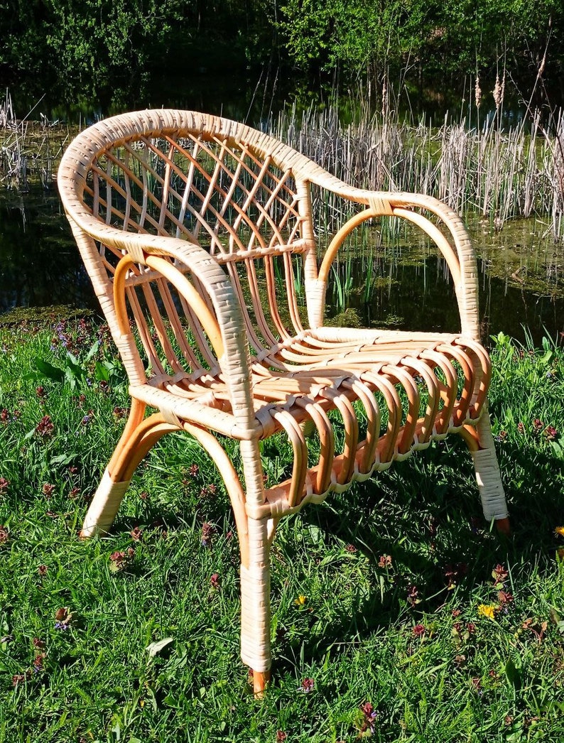 May include: A wicker chair with a woven back and seat. The chair is light brown and has a natural finish. It is sitting on a bed of green grass.