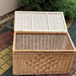 May include: A large, natural woven wicker storage basket with a hinged lid. The basket is open and the lid is propped up, revealing the woven interior.