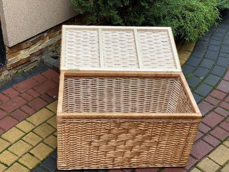 May include: A large, natural woven wicker storage basket with a hinged lid. The basket is open and the lid is propped up, revealing the woven interior.