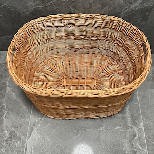 May include: A large, oval-shaped wicker basket with woven handles. The basket is made of natural brown wicker and is empty.