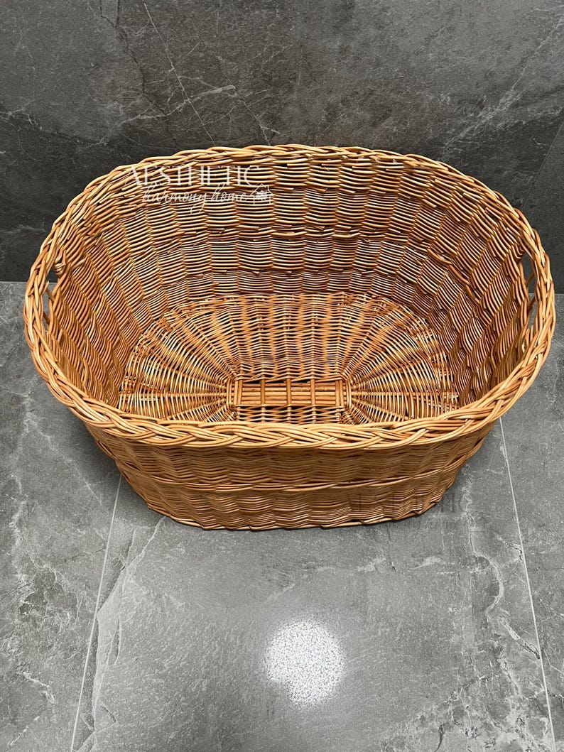 May include: A large, oval-shaped wicker basket with woven handles. The basket is made of natural brown wicker and is empty.