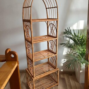 May include: A tall, arched, woven wicker shelf unit with four shelves. The shelf unit is made of natural brown wicker and has a rustic, bohemian style.