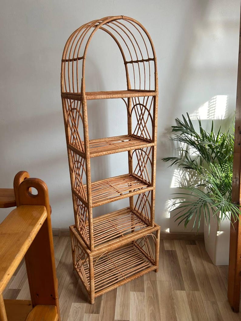 May include: A tall, arched, woven wicker shelf unit with four shelves. The shelf unit is made of natural brown wicker and has a rustic, bohemian style.