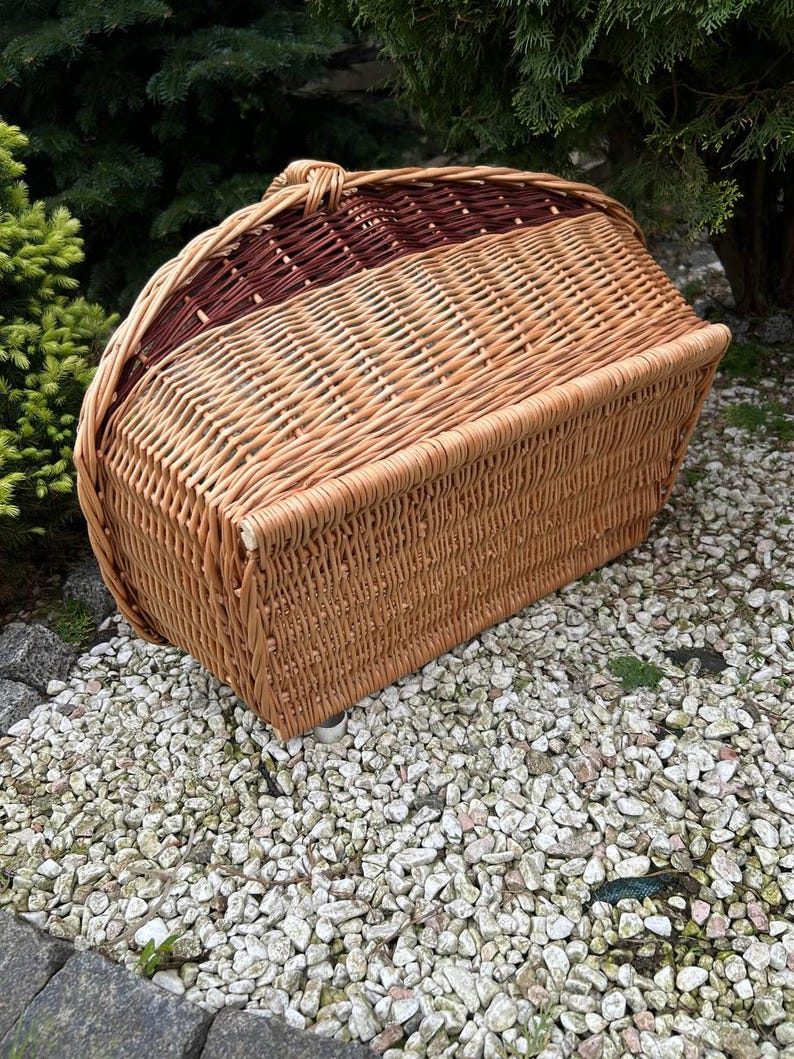 Op de afbeelding: Een grote, geweven rieten mand met een bruin en natuurlijk kleurenschema. De mand heeft een afgeronde bovenkant en een platte bodem. Hij staat op een bed van kleine witte stenen.