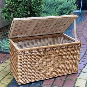 May include: A large, natural woven wicker storage basket with a hinged lid. The basket is made of light brown wicker and has a rectangular shape.