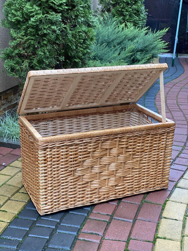 May include: A large, natural woven wicker storage basket with a hinged lid. The basket is made of light brown wicker and has a rectangular shape.