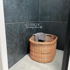 May include: A brown wicker basket with a gray towel inside, sitting in a corner of a bathroom with dark gray tile walls.