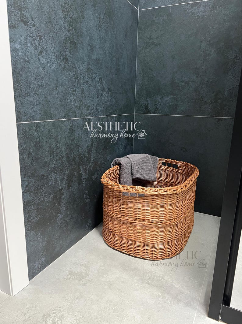 May include: A brown wicker basket with a gray towel inside, sitting in a corner of a bathroom with dark gray tile walls.