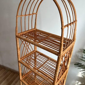 May include: A tall, arched, natural wicker shelf unit with five shelves. The shelf unit is made of woven rattan and has a natural brown color.