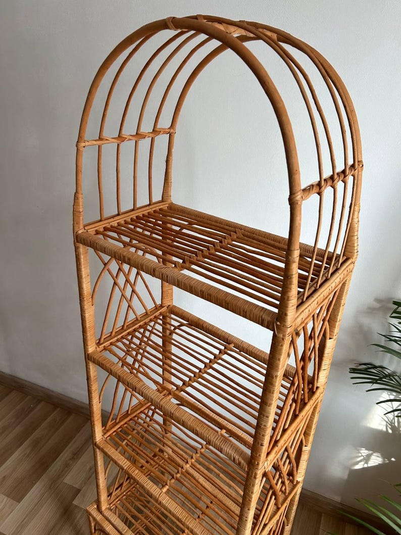 May include: A tall, arched, natural wicker shelf unit with five shelves. The shelf unit is made of woven rattan and has a natural brown color.