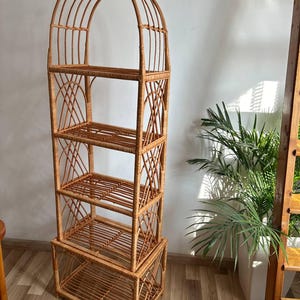 May include: A tall, arched, woven wicker shelf unit with four shelves. The shelf is made of natural brown wicker and has a rustic, bohemian style.