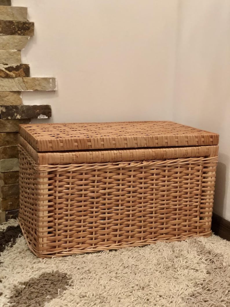 Puede incluir: Una cesta de almacenamiento de mimbre tejido natural con tapa. La cesta es de color marr&oacute;n claro y tiene una forma rectangular.