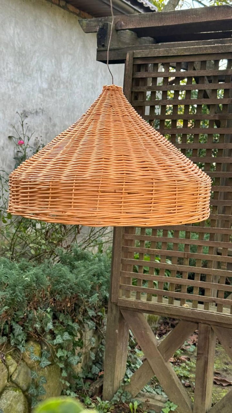 Pu&ograve; includere: Un paralume in vimini intrecciato di colore marrone chiaro, appeso a un soffitto in un ambiente esterno.