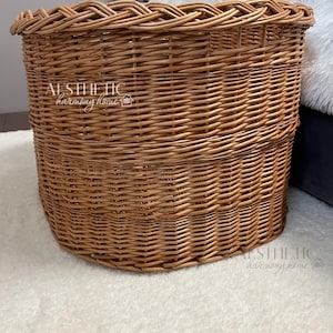 May include: A large, oval-shaped wicker basket with a woven pattern. The basket is made of natural brown wicker and has a slightly rounded bottom.