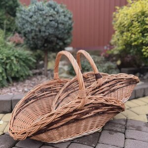 May include: A large, oval-shaped wicker basket featuring a woven light brown and dark brown pattern. The basket has two arched handles that meet in the center, a deep, open-top design, and a sturdy, braided rim construction made of natural willow.