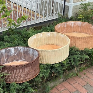 May include: Three round, shallow baskets made of woven material in varying shades of brown, light tan, and natural beige. Each basket features a flat wooden base and a clear plastic liner covering the interior walls, designed for holding items.
