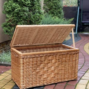 May include: A large, natural woven wicker storage basket with a hinged lid. The basket is open and the lid is propped up, revealing the empty interior.