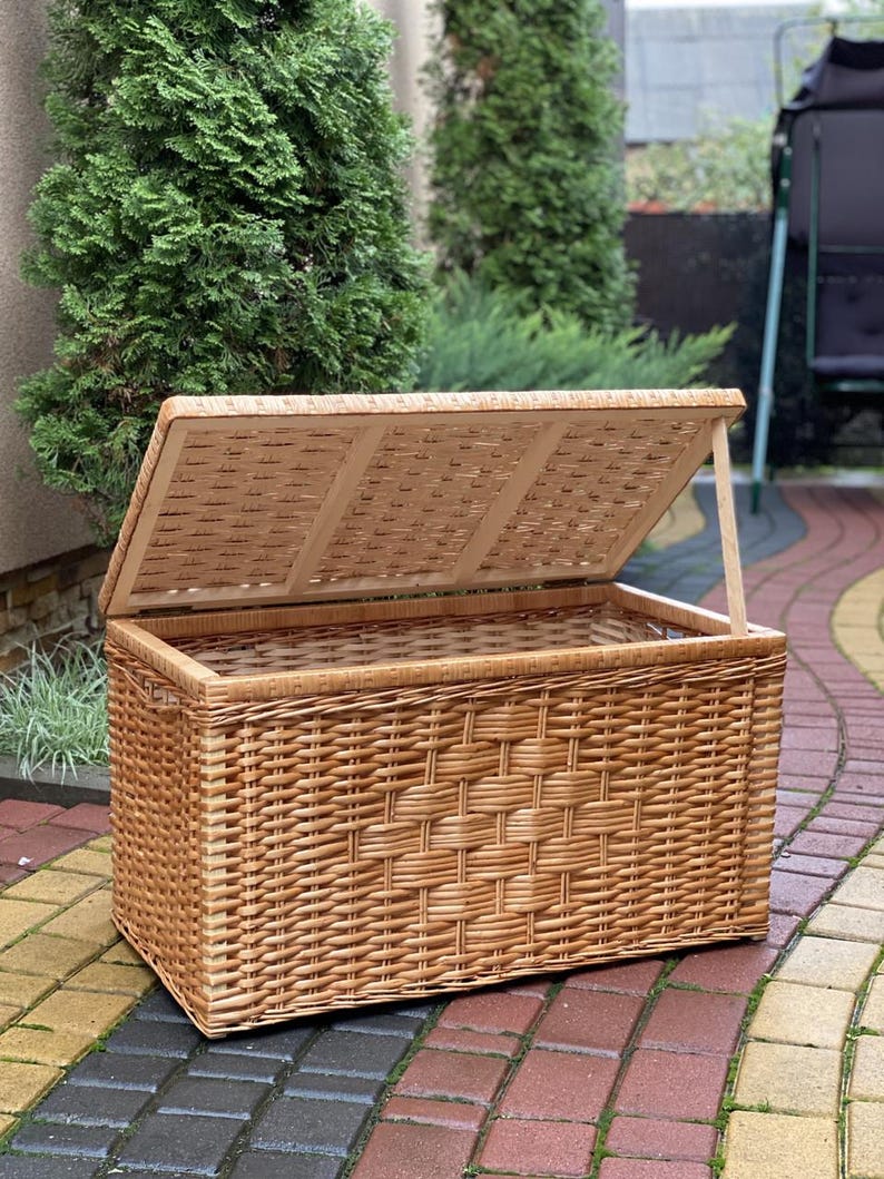 May include: A large, natural woven wicker storage basket with a hinged lid. The basket is open and the lid is propped up, revealing the empty interior.