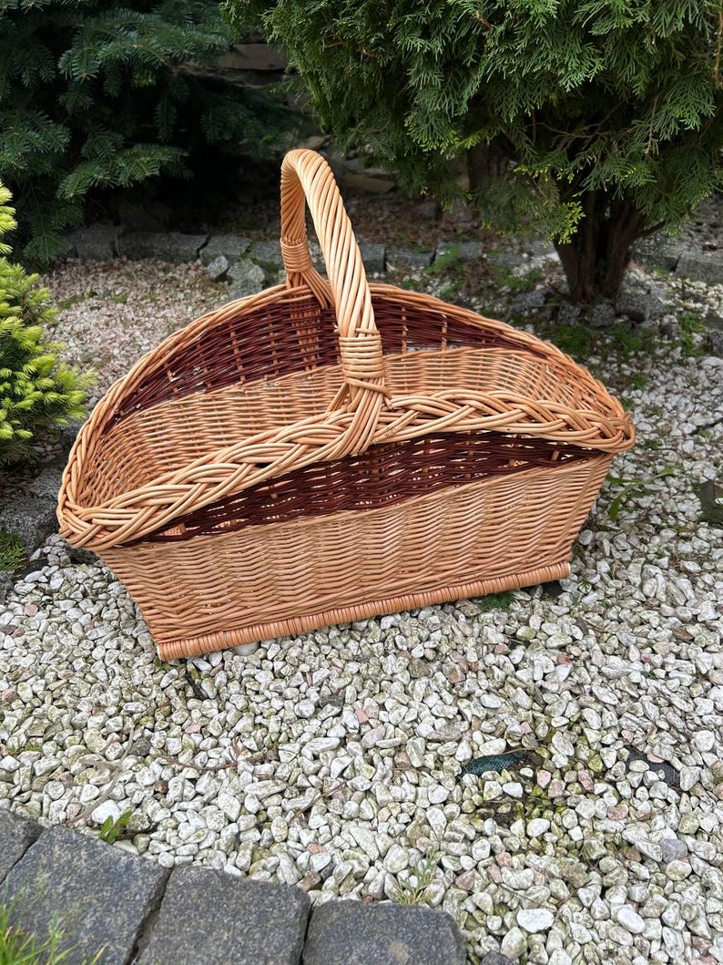 Op de afbeelding: Een geweven rieten mand met een bruin en natuurlijke kleurschema. De mand heeft een handvat en is ontworpen om houtblokken te dragen.