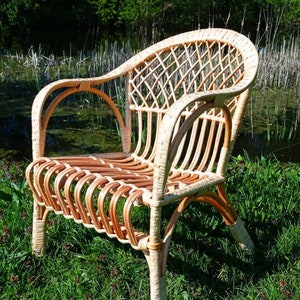 May include: A wicker chair with a woven back and seat. The chair is light brown and has a natural finish. It is sitting on a bed of green grass.