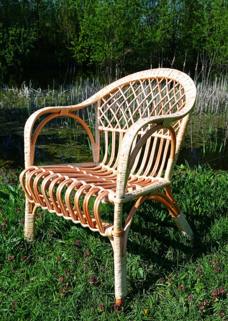 May include: A wicker chair with a woven back and seat. The chair is light brown and has a natural finish. It is sitting on a bed of green grass.