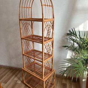 May include: A tall, arched, natural woven rattan shelf unit with four shelves. The shelf unit has a natural wood finish and is made of woven rattan.