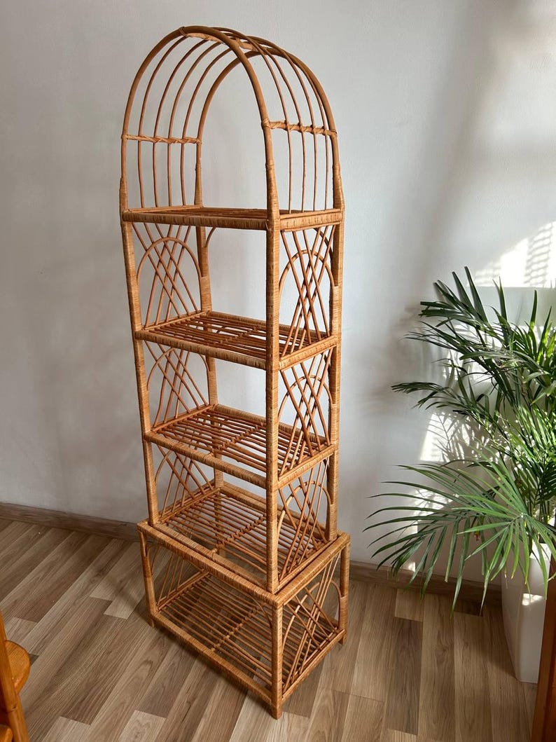 May include: A tall, arched, natural woven rattan shelf unit with four shelves. The shelf unit has a natural wood finish and is made of woven rattan.