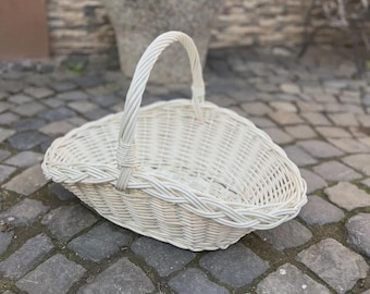 May include: A white woven wicker basket featuring an oval-shaped base and a single arched handle. The basket is constructed with a braided rim detail and a sturdy, open-weave design, providing a lightweight and functional container for various items.