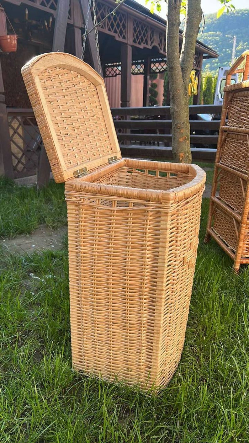 May include: A natural woven wicker storage basket with a hinged lid. The basket is light brown and has a rectangular shape. The basket is sitting on a bed of green grass.