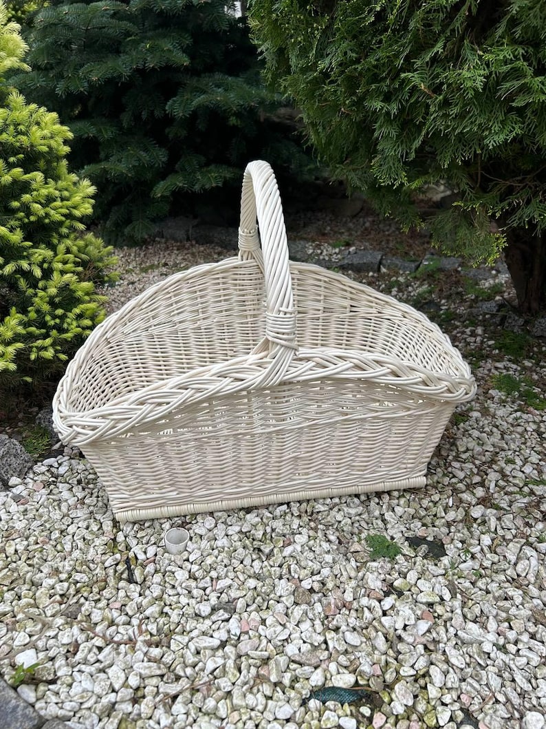 Op de afbeelding: Een witte rieten mand met een handvat. De mand is ovaalvormig en heeft een geweven ontwerp. De mand staat op een bed van kleine witte stenen.