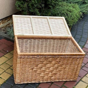 May include: A woven wicker storage basket with a lid. The basket is light brown and has a diamond pattern on the front. The lid is open and shows the woven interior.