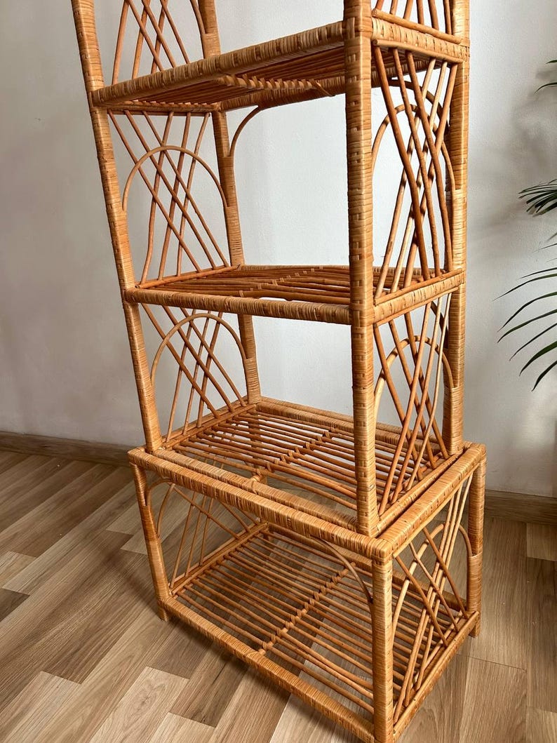 May include: A tall, natural woven wicker shelf unit with four shelves. The shelf unit is made of light brown wicker and has a geometric design.