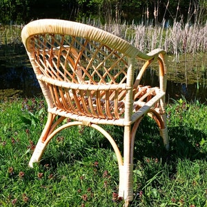 May include: A wicker chair with a woven back and seat, sitting on a bed of green grass with small pink flowers.