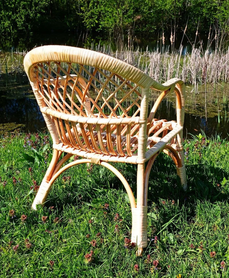 May include: A wicker chair with a woven back and seat, sitting on a bed of green grass with small pink flowers.
