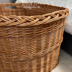 May include: A large, round, natural woven wicker basket with a braided rim. The basket has two cut-out handles on the side. The text "AESTHETIC harmony home" is printed on the top rim of the basket.