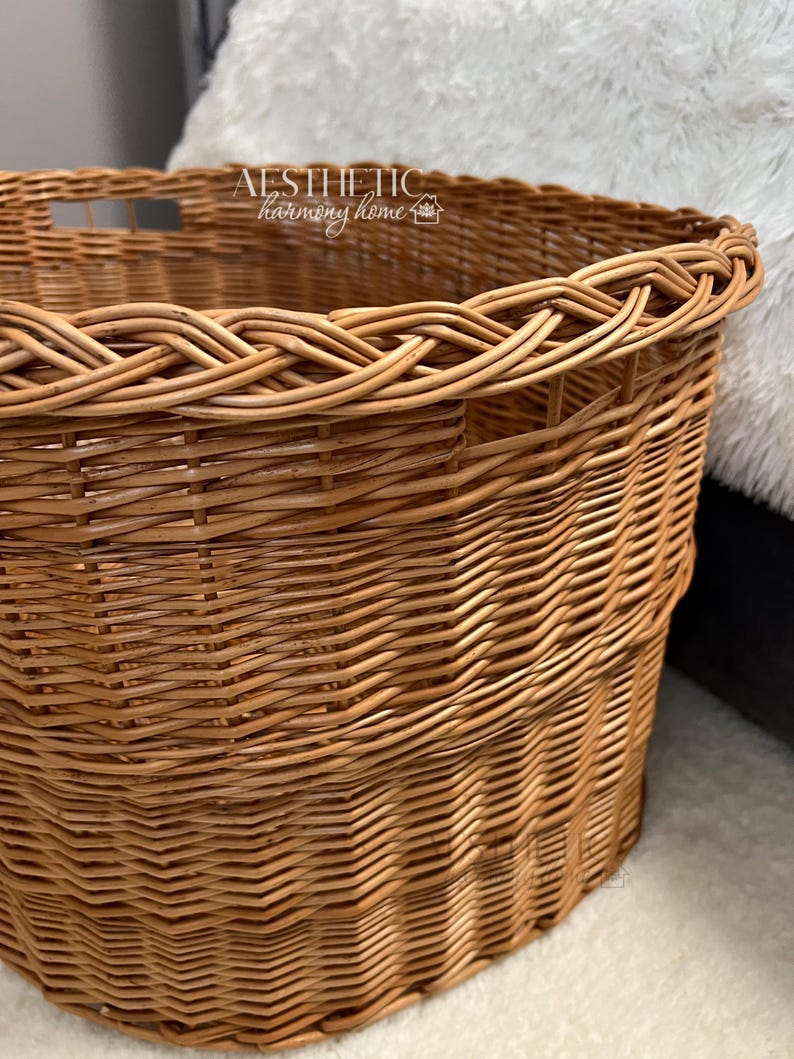 May include: A large, round, natural woven wicker basket with a braided rim. The basket has two cut-out handles on the side. The text "AESTHETIC harmony home" is printed on the top rim of the basket.
